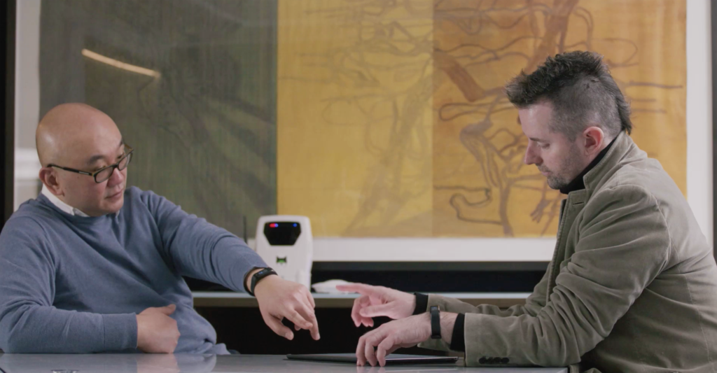 2 handsome men sitting at a conference room table talking and looking at a tablet